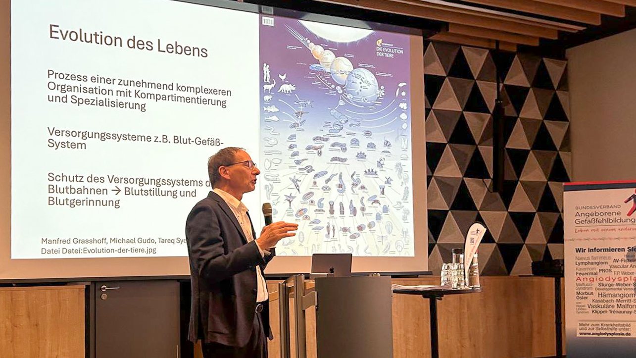 Un intervenant parle au micro devant un écran affichant la diapositive « Evolution des Lebens ».